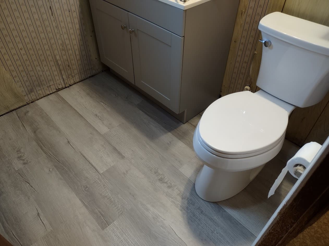 Finished gray wood-look vinyl plank floor with the new toilet and vanity in place, looking down across the room