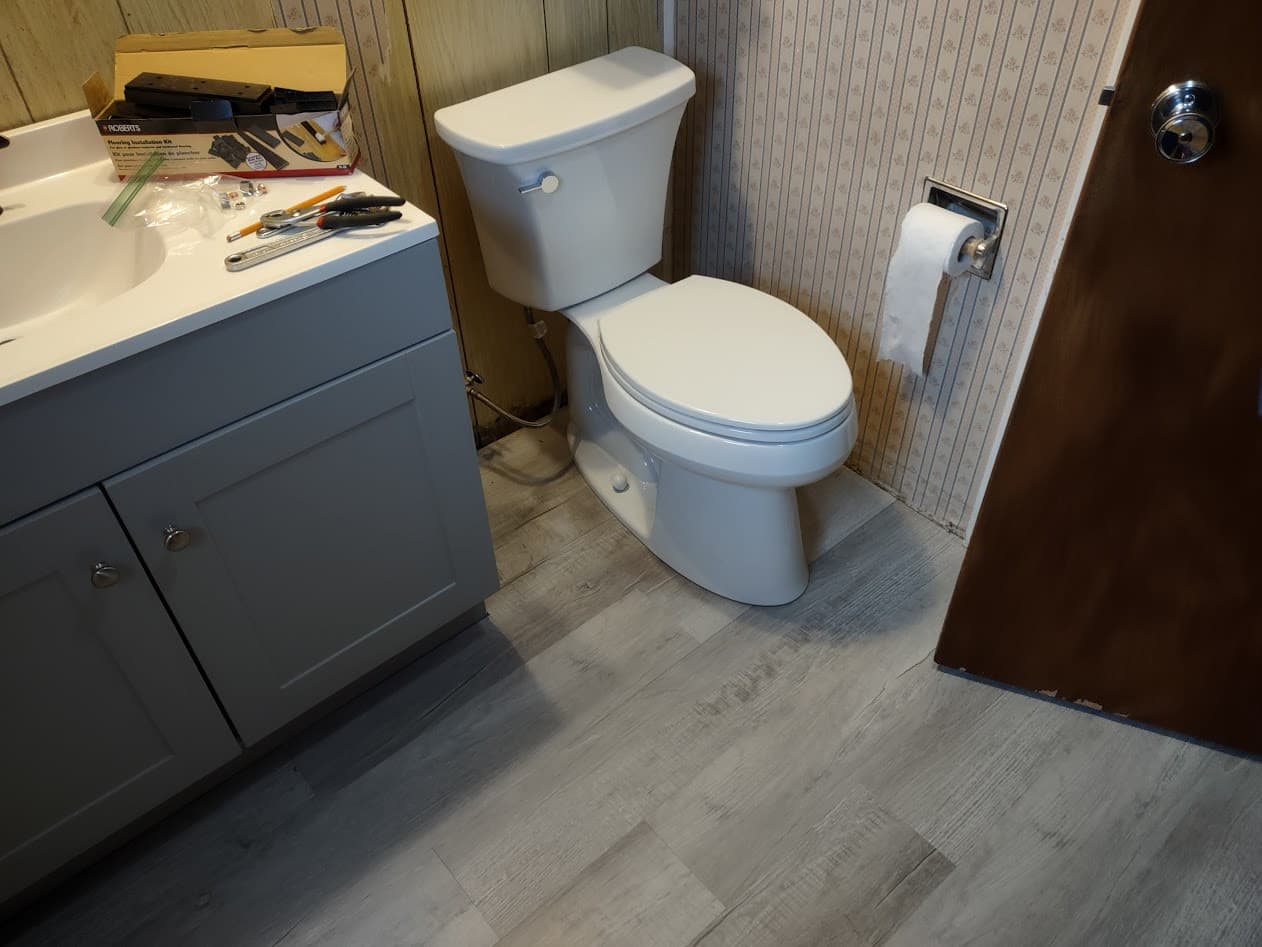 The new toilet set on the fresh vinyl plank floor, with the flooring installation kit and tools on the new vanity