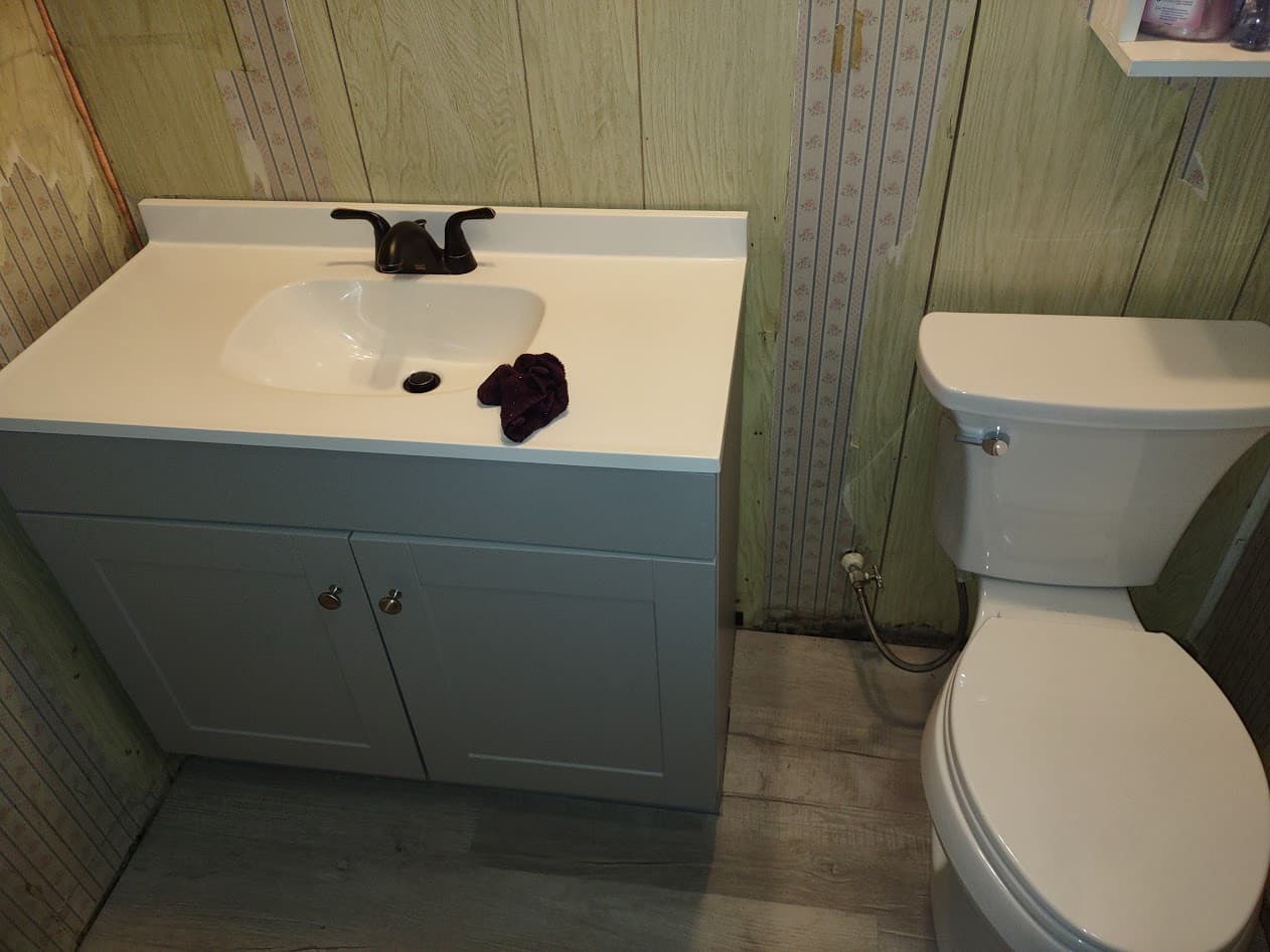 The new gray vanity with a one-piece integrated-sink top and oil-rubbed bronze faucet beside the new toilet on the finished vinyl floor