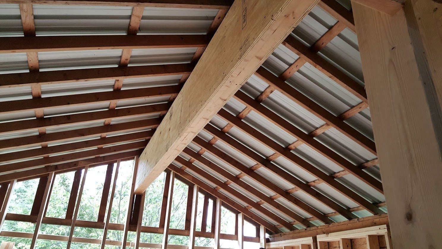Site-built plywood box beam carrying the roof framing up to the ridge in a vaulted, metal-roofed structure