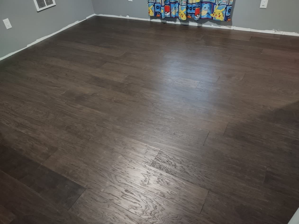 The finished dark hardwood floor laid wall to wall with staggered plank seams