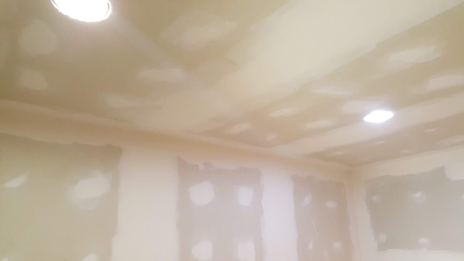 Skim-coated drywall ceiling with joint compound feathered over the seams and fasteners, recessed lights set in