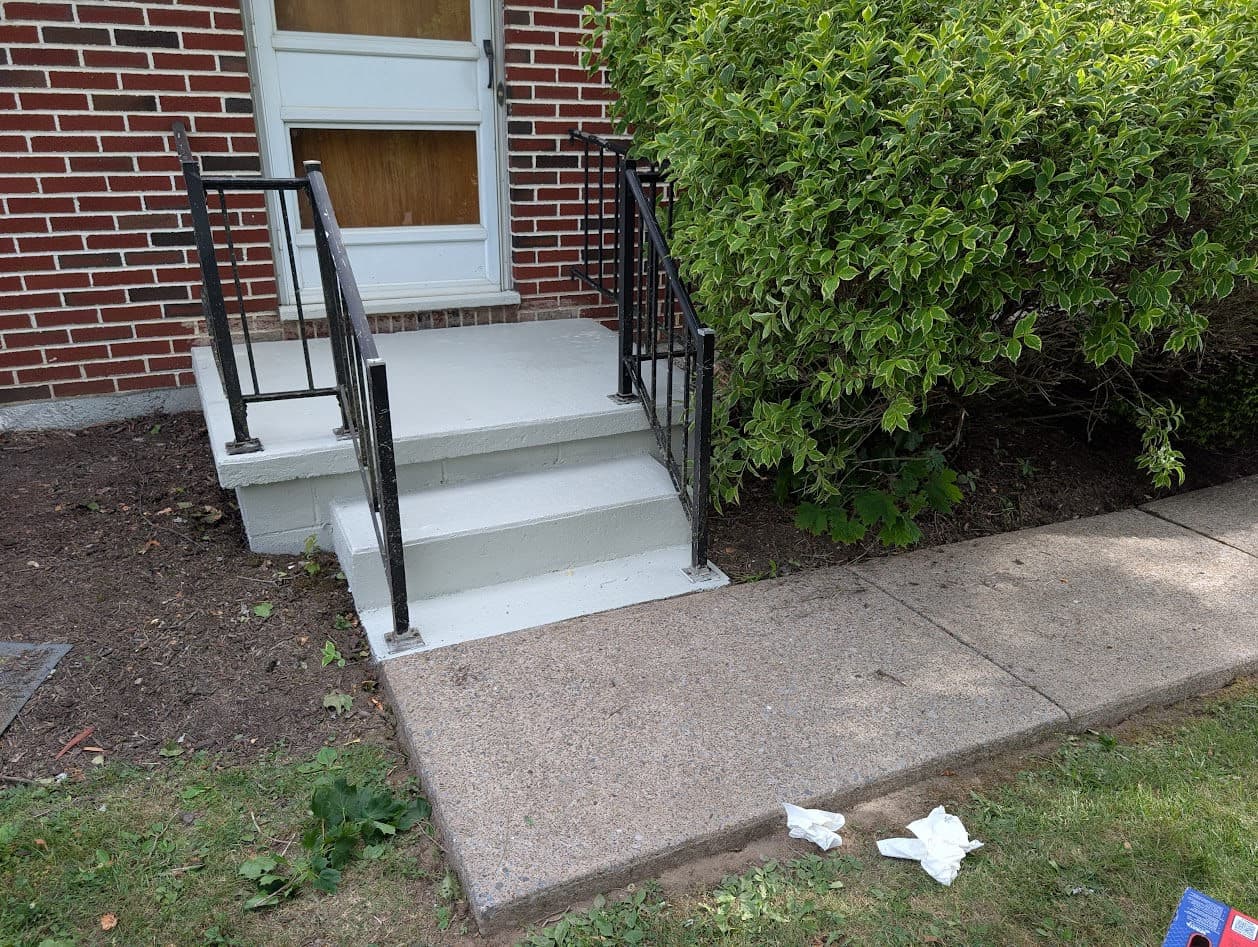 The finished stoop and steps repainted in a clean light gray with two coats, beside the freshly cleaned sidewalk