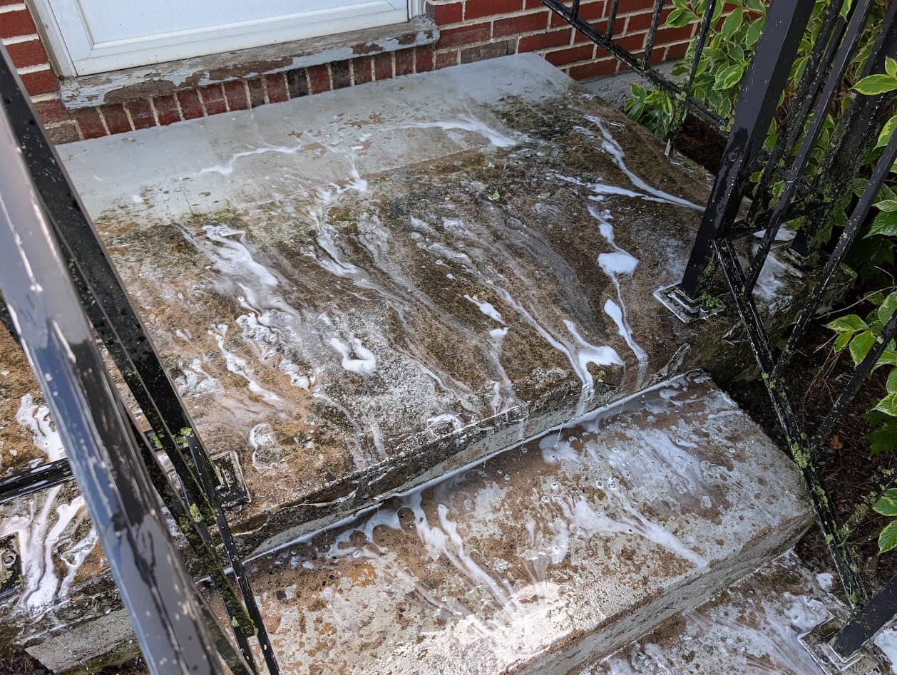 Pressure-washing the entry stoop and steps, cleaner and suds running off as the algae and grime lift away