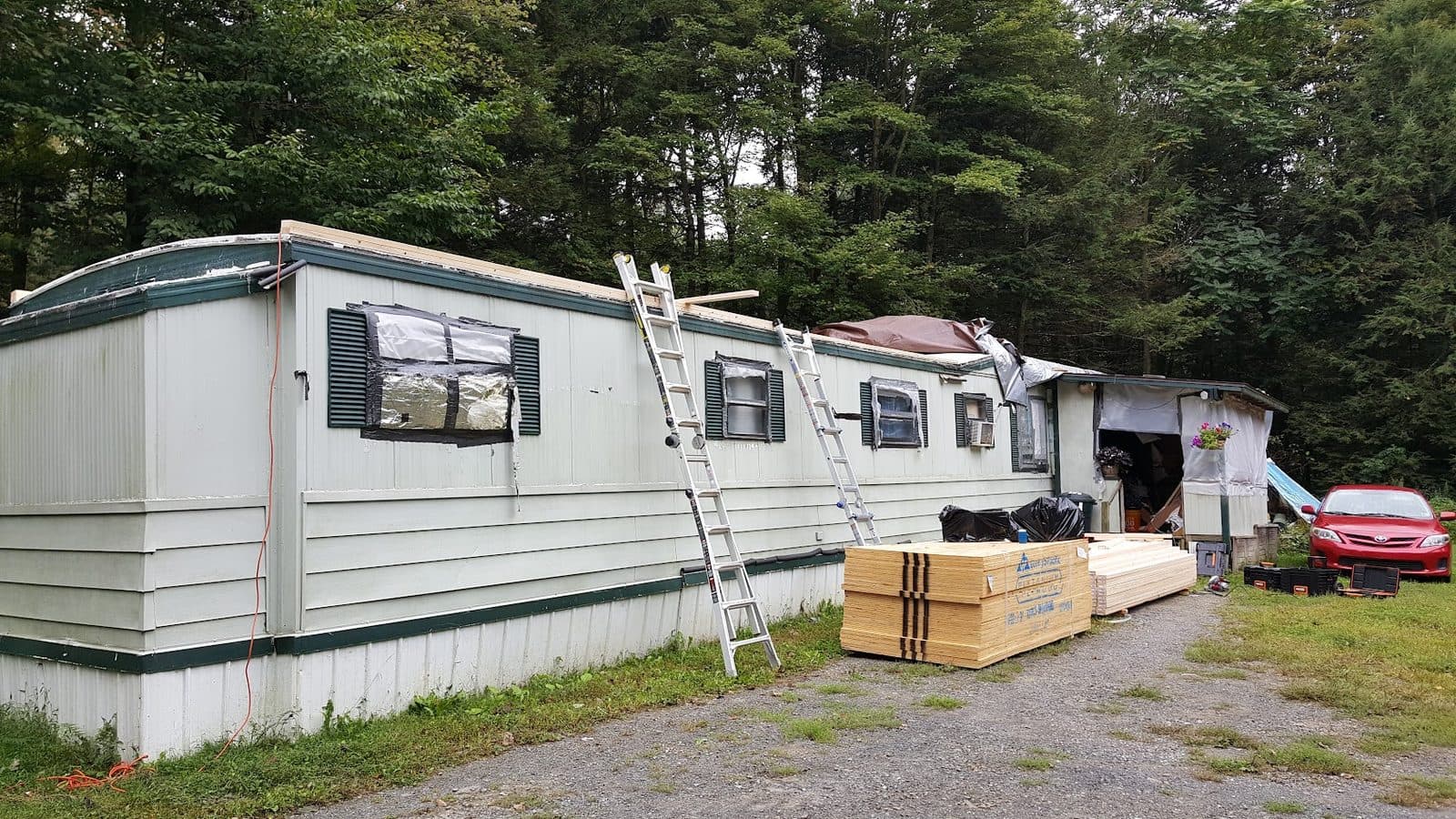 Mobile home with its failing original roof before the roof-over, with materials staged on site