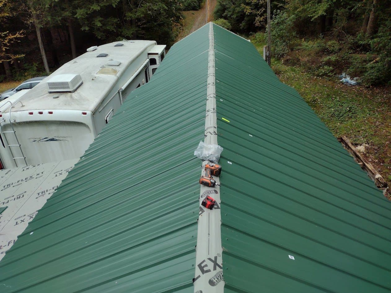 Green ribbed metal roofing being installed over Tri-Flex underlayment on the new truss roof