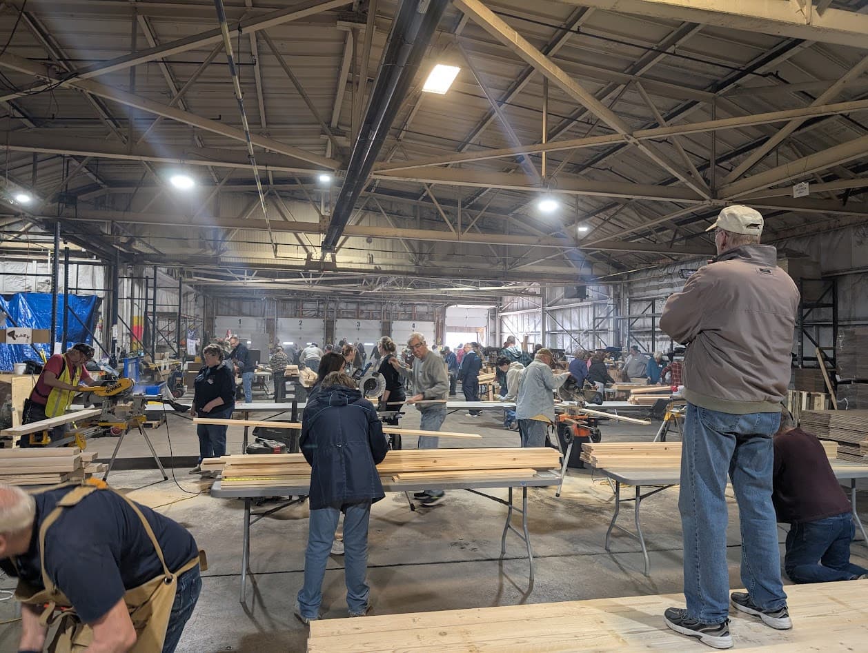 Volunteers at work across the build floor, cutting and sorting lumber at miter-saw stations