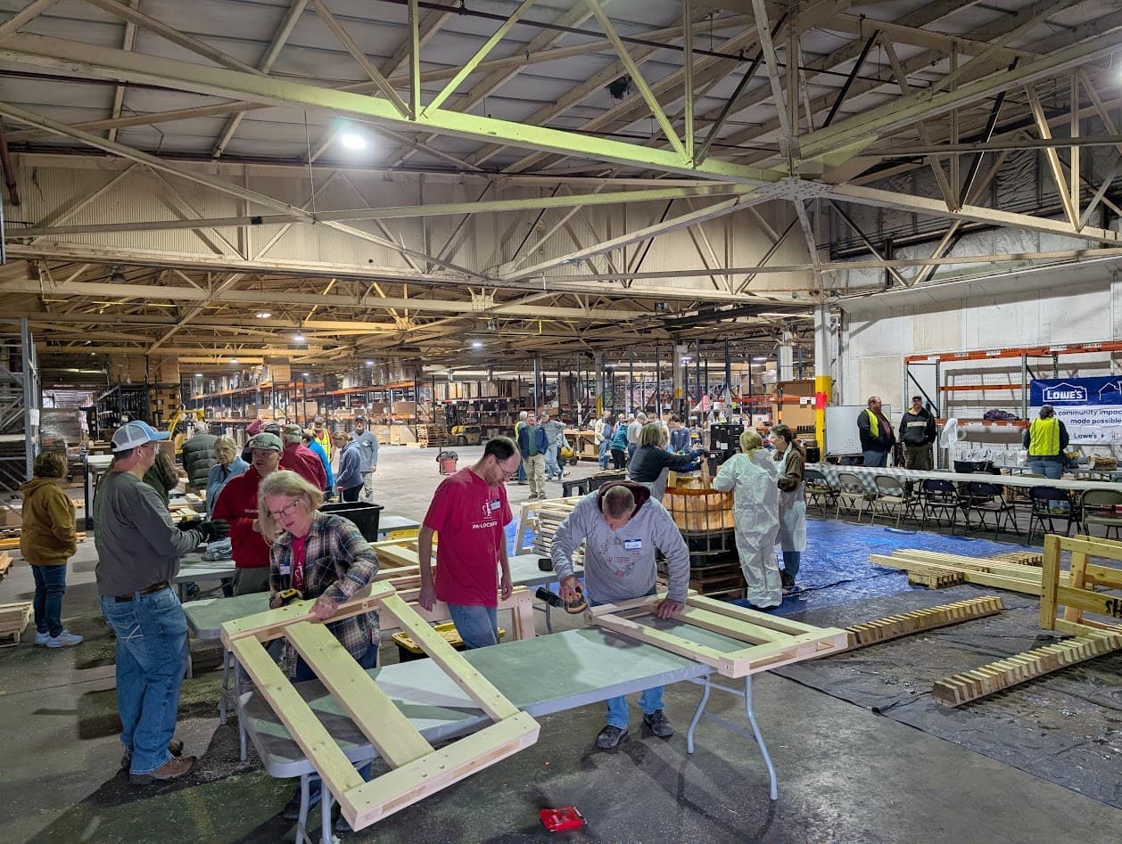 Volunteers filling the build floor, assembling bed frames at tables across the warehouse
